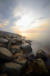 Rocks at sea shore against sky during sunset