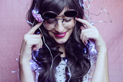 Close-up of smiling female model with illuminated string lights against peach backdrop