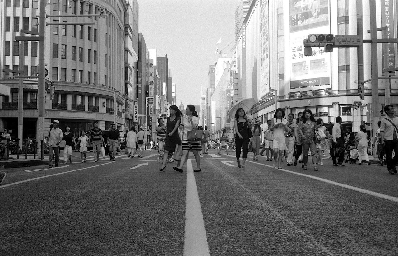 building exterior, architecture, city, built structure, transportation, street, large group of people, men, city life, walking, person, road marking, road, city street, lifestyles, the way forward, mode of transport, car, land vehicle