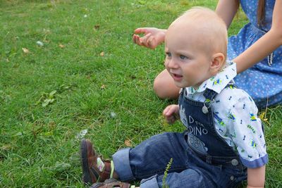 Cute baby boy sitting with mother on grassy field