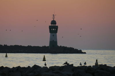 View of lighthouse by sea against sky during sunset