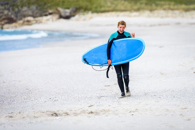 Portrait of happy woman with surfboard walking at sandy beach