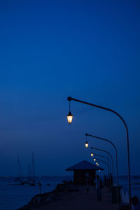Illuminated street light by sea against clear sky at dusk