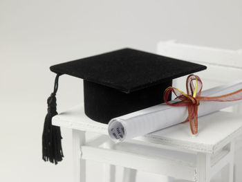 Mortarboard and diploma on table with chair against white background