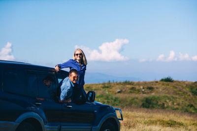 Woman sitting on car against sky