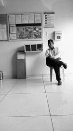 Full length of young man sitting on tiled floor