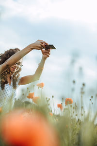 Woman photographing flowering plants against sky
