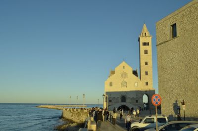 People on building by sea against clear blue sky