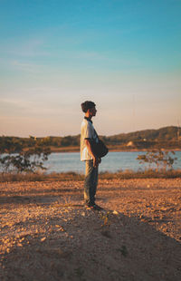 Man standing on lakeshore against sky during sunset