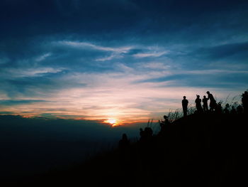 Silhouette people at mountain peak against sky during sunset