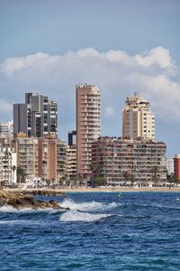 Scenic view of sea against city and cloudy sky