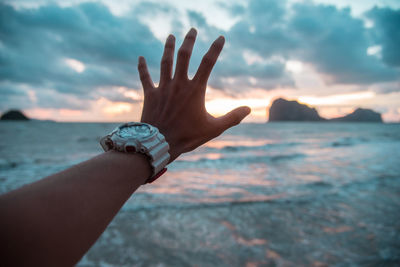 Cropped hand of man wearing wristwatch gesturing against sea and sky