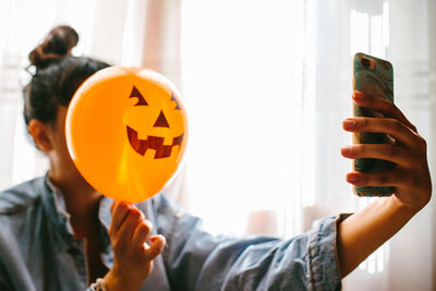 Close-up of woman holding halloween decoration against face and taking selfie at home