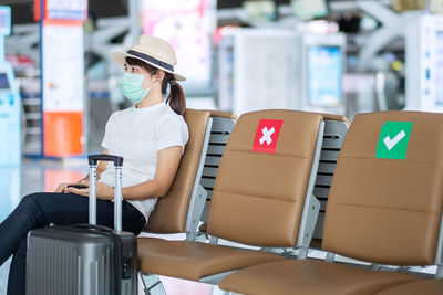 Woman wearing mask with luggage sitting in airport