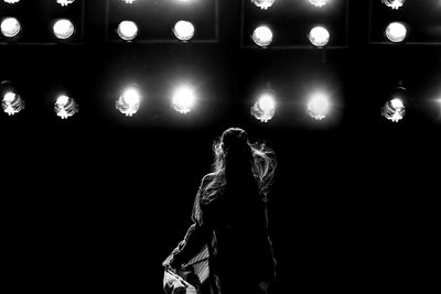 Rear view of person standing against illuminated lights at night