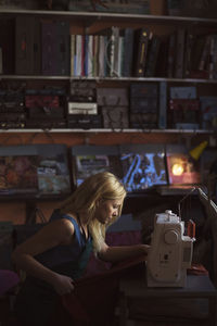 Side view of young female fashion designer using sewing machine in studio