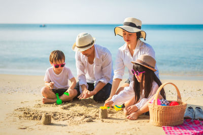 Cheerful family building sandcastle on beach against sea