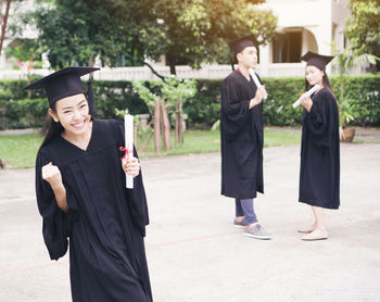 Cheerful student with clenched fist wearing graduation gown