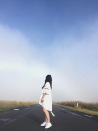 Side view of woman standing on country road against sky