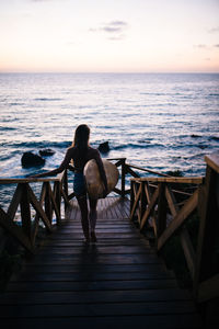 Woman walking on jetty at beach against sky during sunset