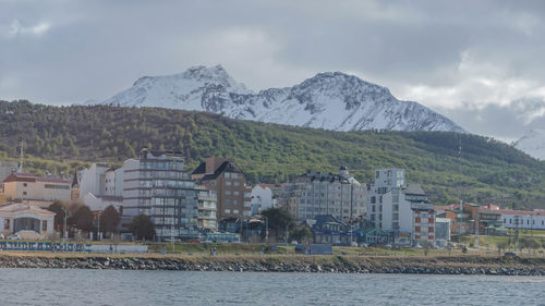 Houses by river and buildings against sky in city