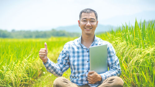 Portrait of smiling man holding laptop in field