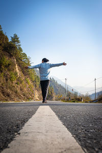 Young girl standing at the center of tarmac road from low angle at morning