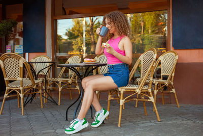 Young attractive curly woman sits at table in cafe on summer terrace. colorful delicious donuts, 