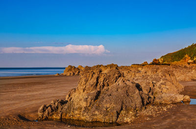 Rock formations on beach against blue sky