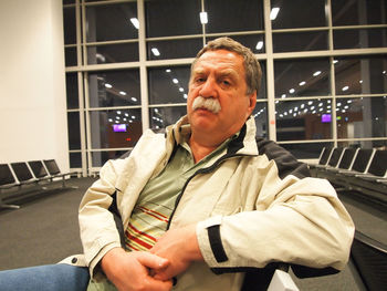 Portrait of senior man sitting on chair at airport departure area