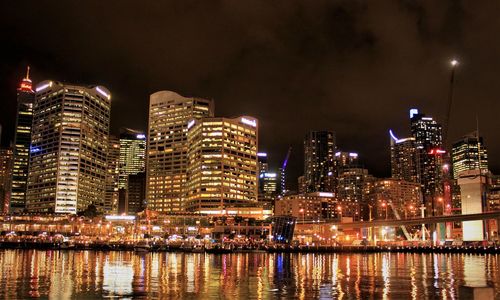 Illuminated buildings by river against sky at night