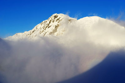 Low angle view of snowcapped mountains against clear blue sky