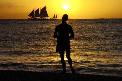 Silhouette man standing in sea against sky during sunset
