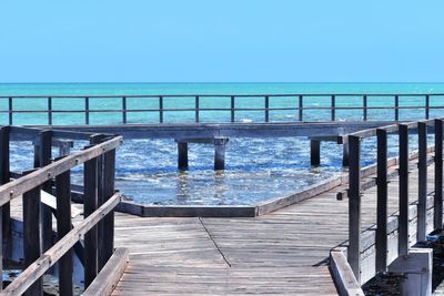 Pier over sea against clear blue sky