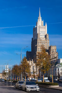 Cars on road by buildings against blue sky