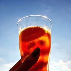 Close-up of hand holding beer glass against sky