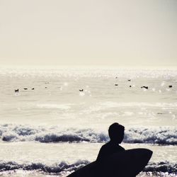 Rear view of silhouette man flying at beach against clear sky