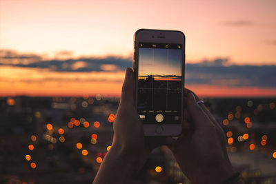 Close-up of hand holding smart phone against sky during sunset