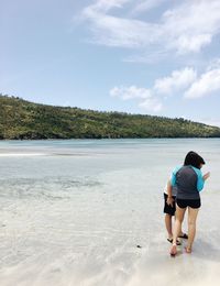 Rear view of woman standing on beach against sky