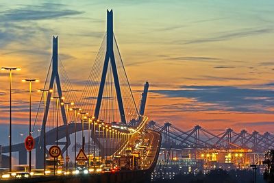 Cars moving on illuminated kohlbrand bridge against cloudy sky during sunset