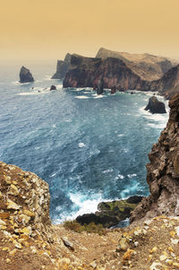 High angle view of rocky coastal feature against clouds