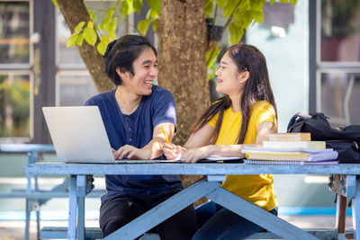 Couple of students sitting and using laptop in outdoor university doing some online research