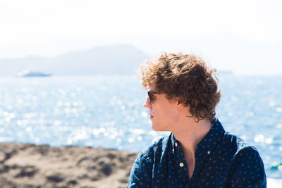 Young man with curly hair against sea on sunny day