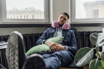 Businessman with neck pillow relaxing on chair in office