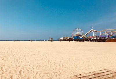 Amusement park by sea against clear blue sky