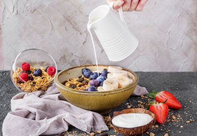 Cropped hand pouring milk in bowl with fruits