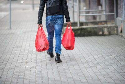 Low section of man carrying plastic bags while walking on sidewalk