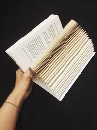 Cropped hand holding book against black background