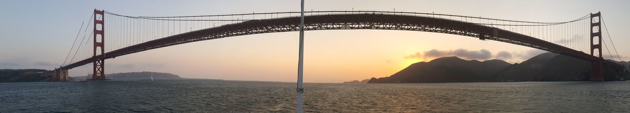 Suspension bridge over sea against sky during sunset