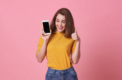 Young woman showing mobile phone while standing against pink background